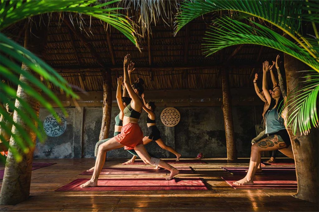 A group of yogis practice Warrior Pose at sunset together in Alive Beach House's tropical outdoor yoga studio in Nicaragua