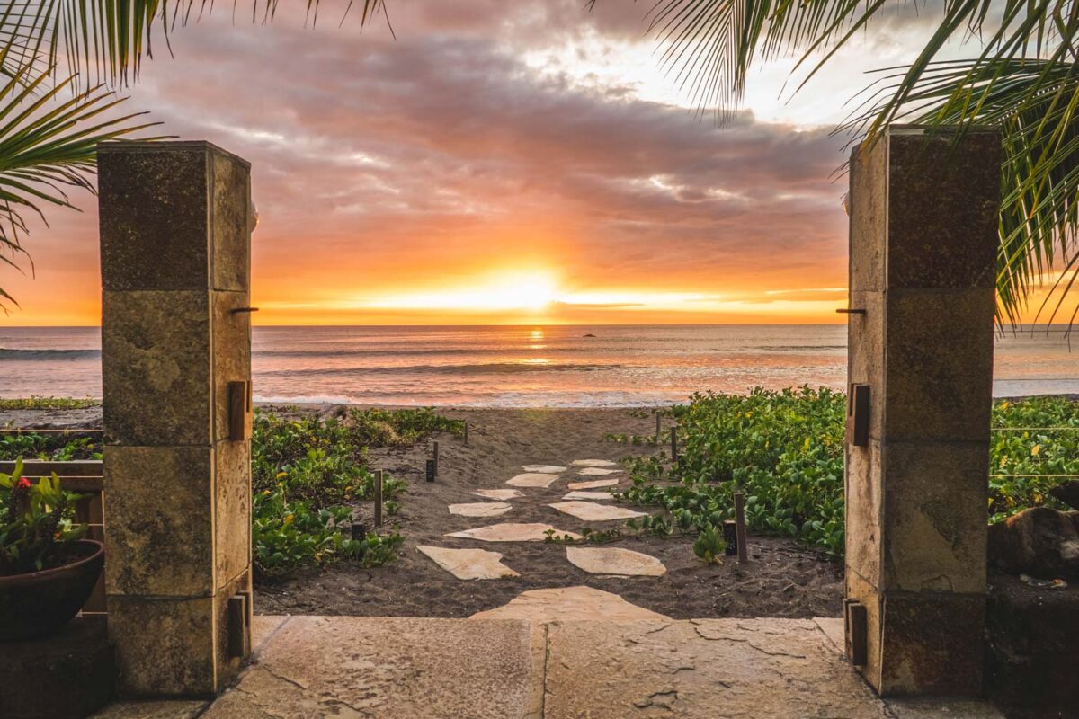 The sun sets against a pink sky beyond the gates of Alive Beach House hotel in El Transito Nicaragua