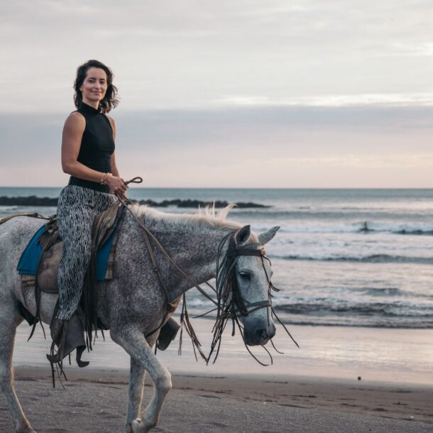 Woman horseback riding on the beach in El Tránsito, Nicaragua, with ocean waves at sunset near Alive Beach House